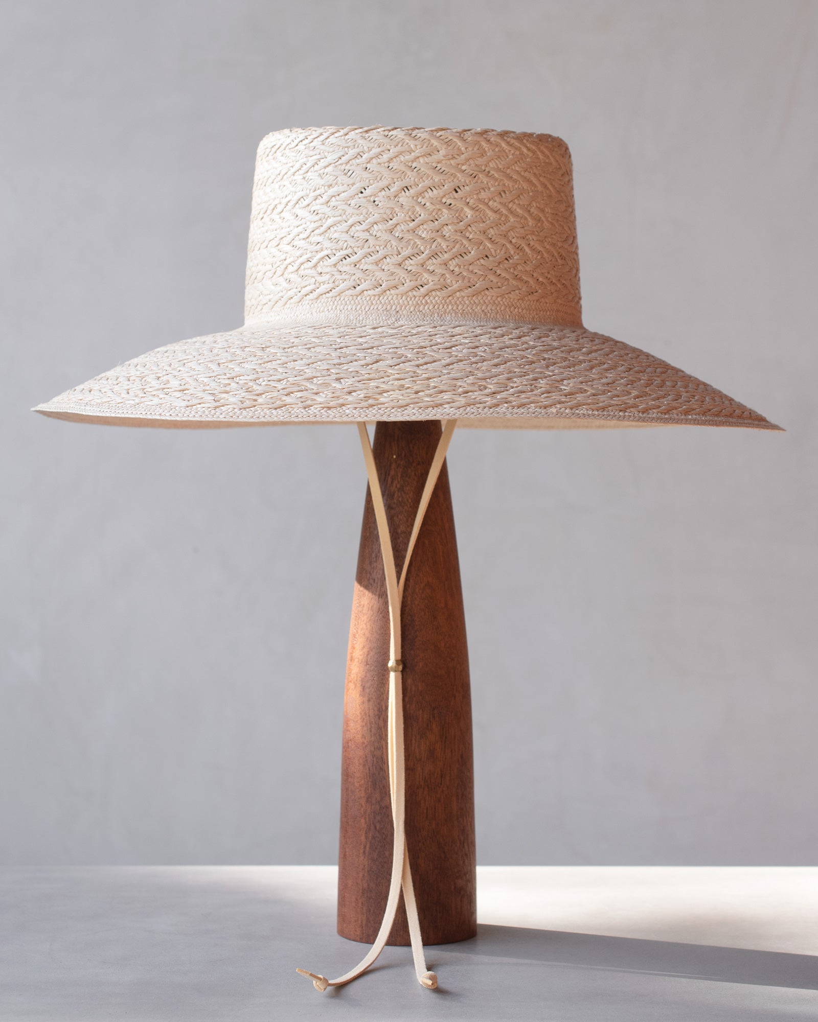 Woven straw hat with wooden base on a gray background
