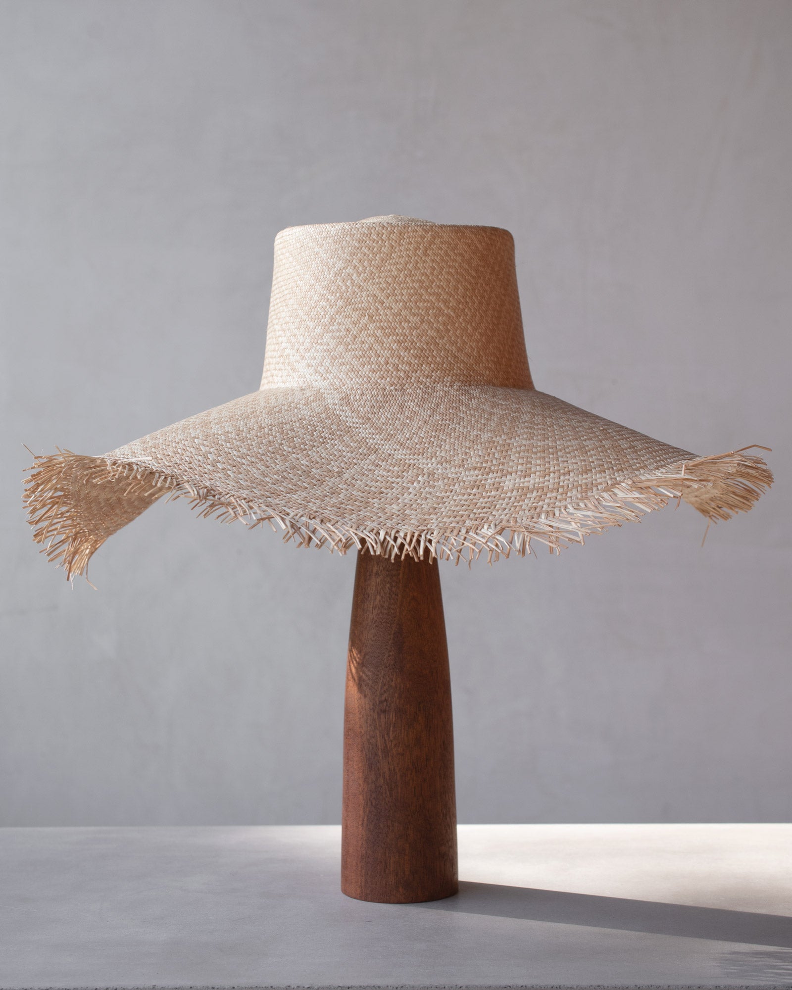 Woven straw hat on a wooden stand against a gray background